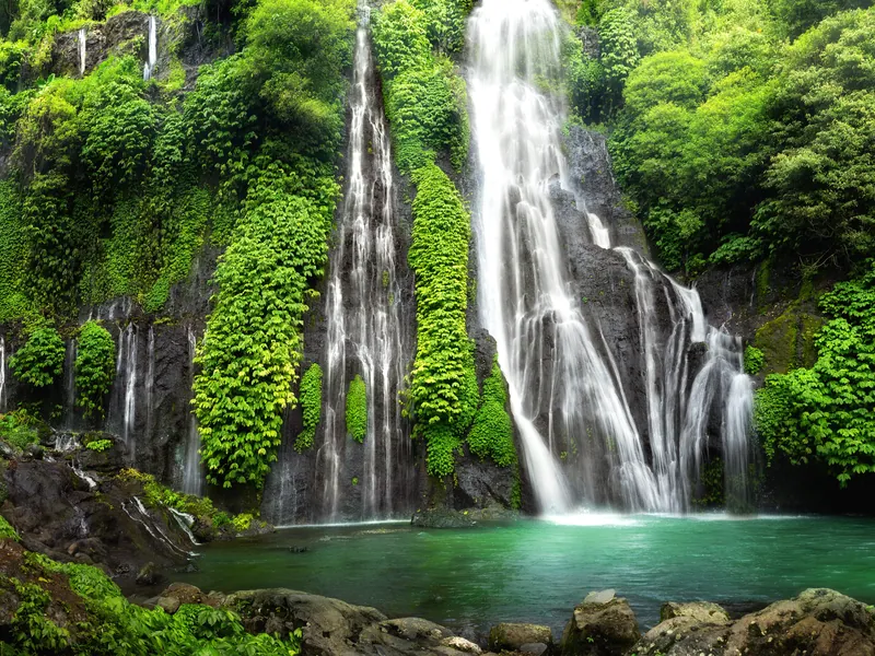The twin Banyumala waterfalls falling into a green pool in dense jungle
