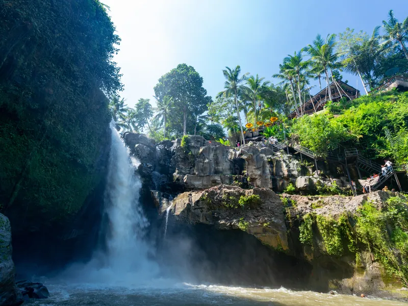 The wide Tegenungan waterfall dropping into a river surrounded by palms