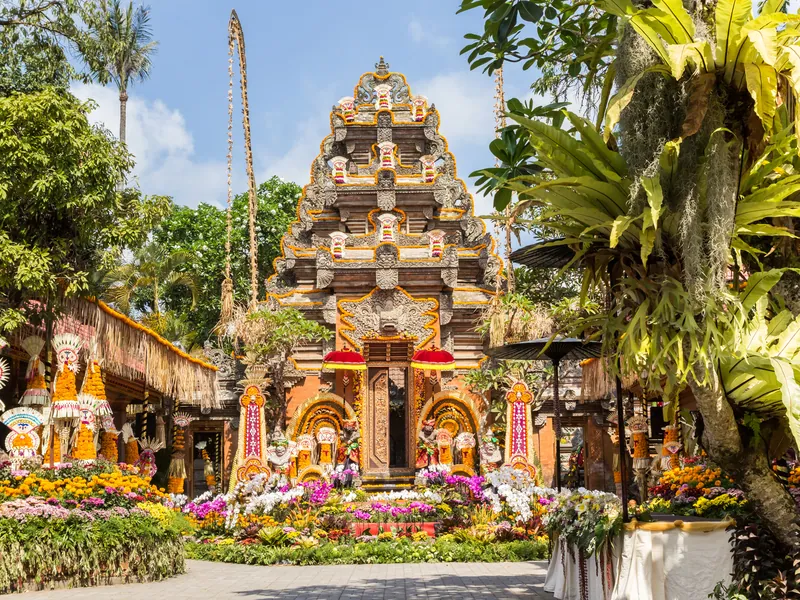 An ornate Balinese temple gate with red offerings and flowers