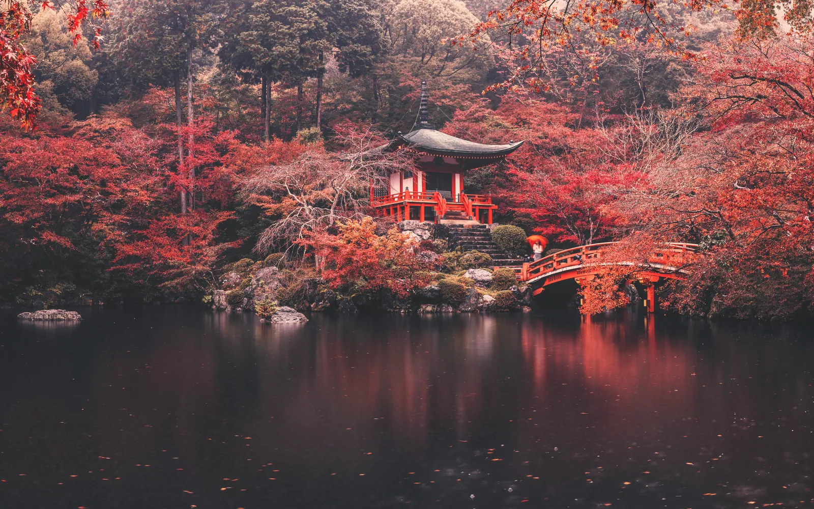 A temple pond ringed by red and orange maples in autumn