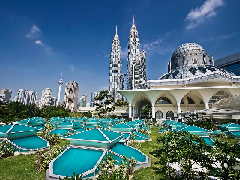 A white mosque with the Petronas Towers rising behind it