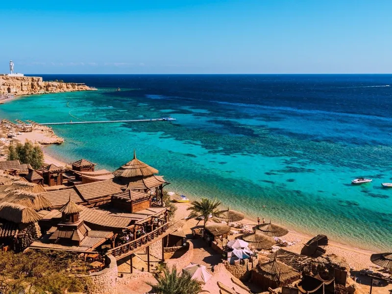 Thatched shelters along a beach beside clear Red Sea water