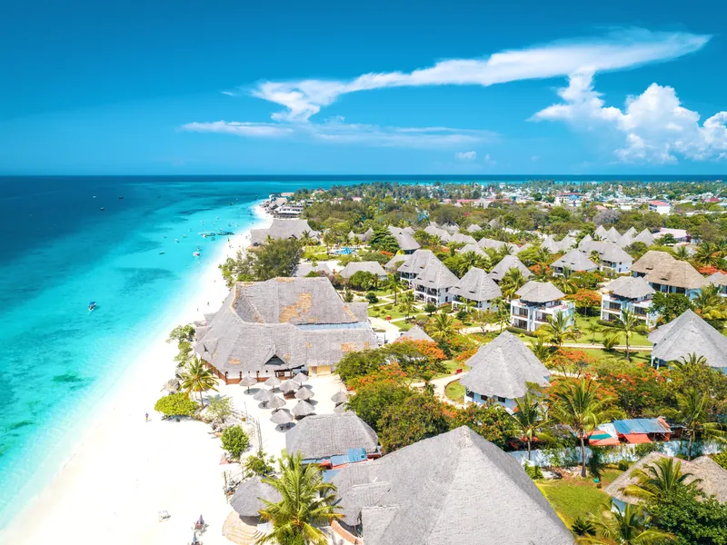 Thatched roofs and palms above a white beach and turquoise water